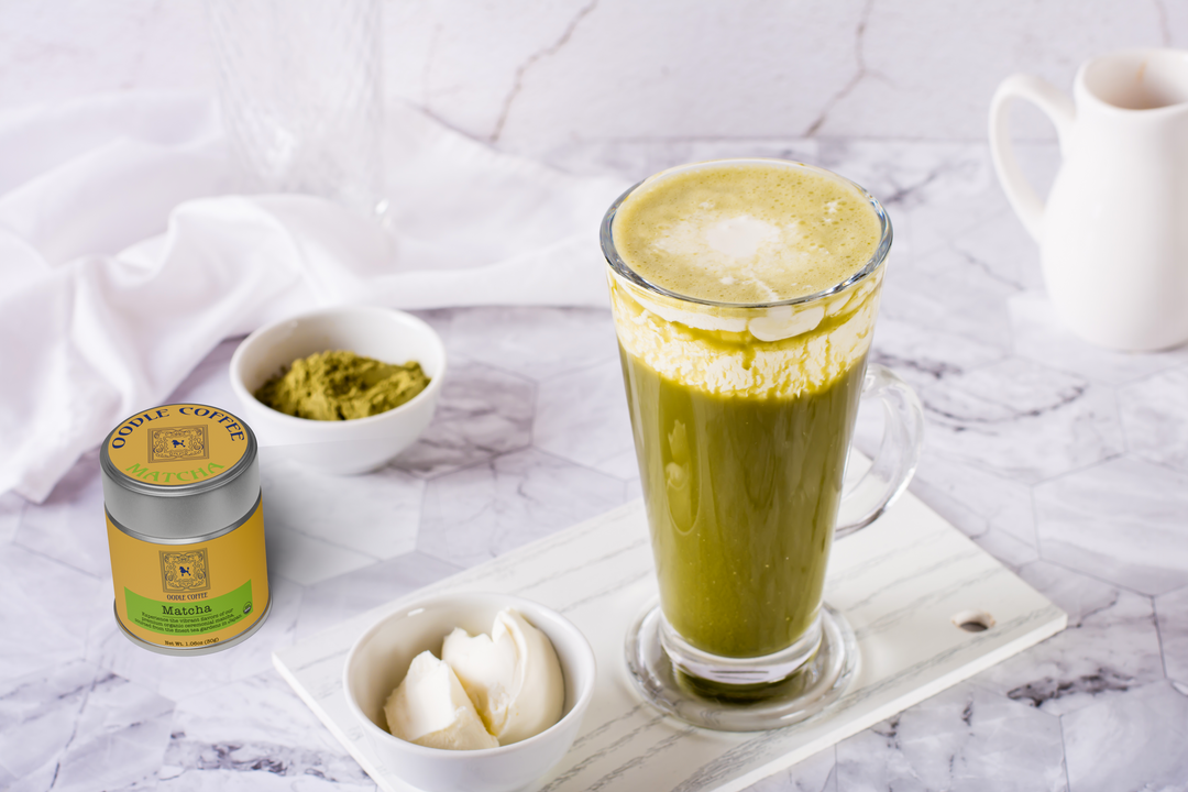 Matcha latte with matcha powder, cream, and a canister on a marble surface