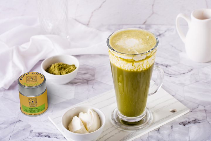 Matcha latte with matcha powder, cream, and a canister on a marble surface